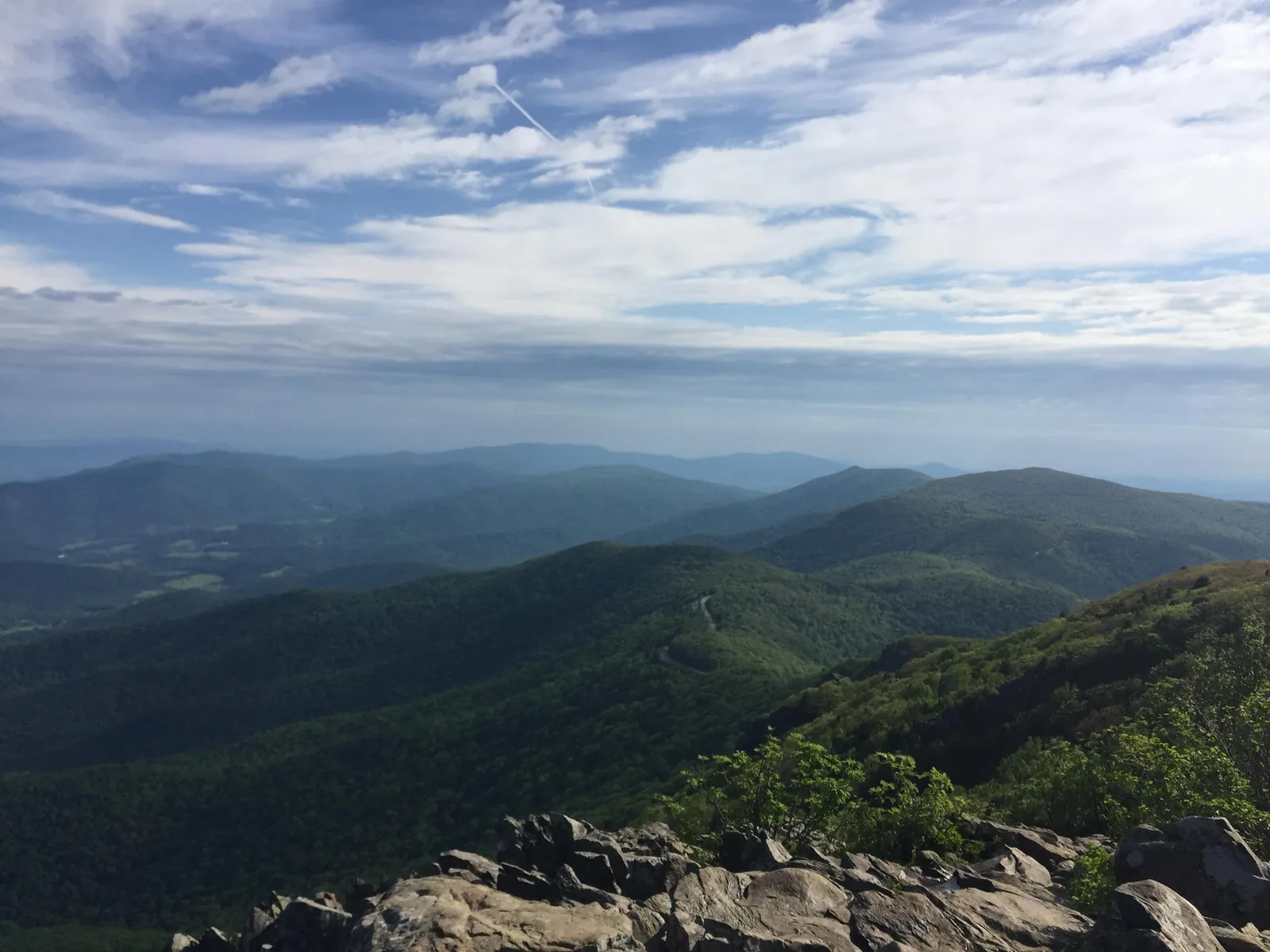 Layered Blue Ridge mountain ridges beneath a bright sky, with rocks in the foreground.