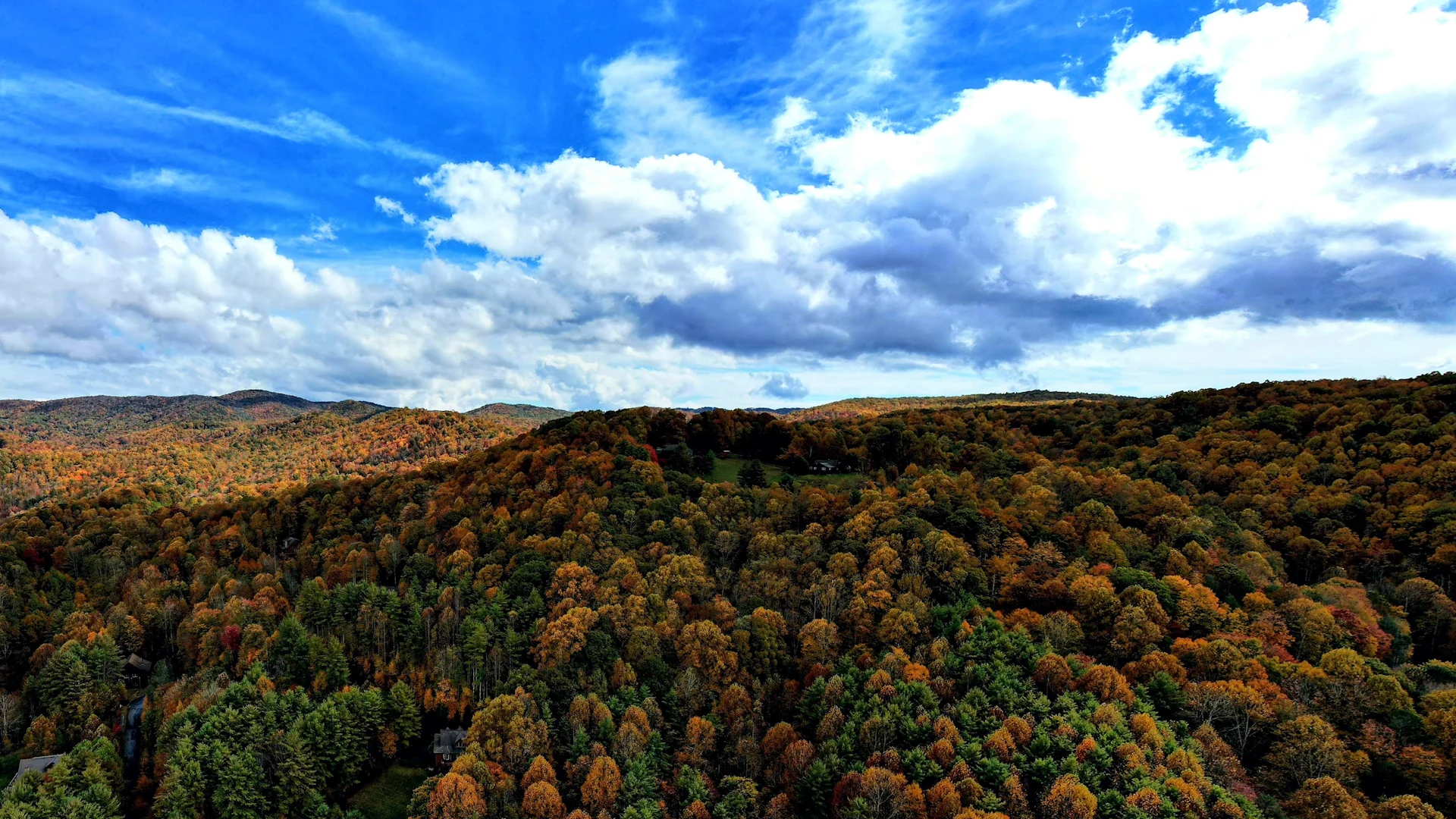 Panoramic Blue Ridge mountain landscape with autumn forest beneath a bright blue, cloud-filled sky.