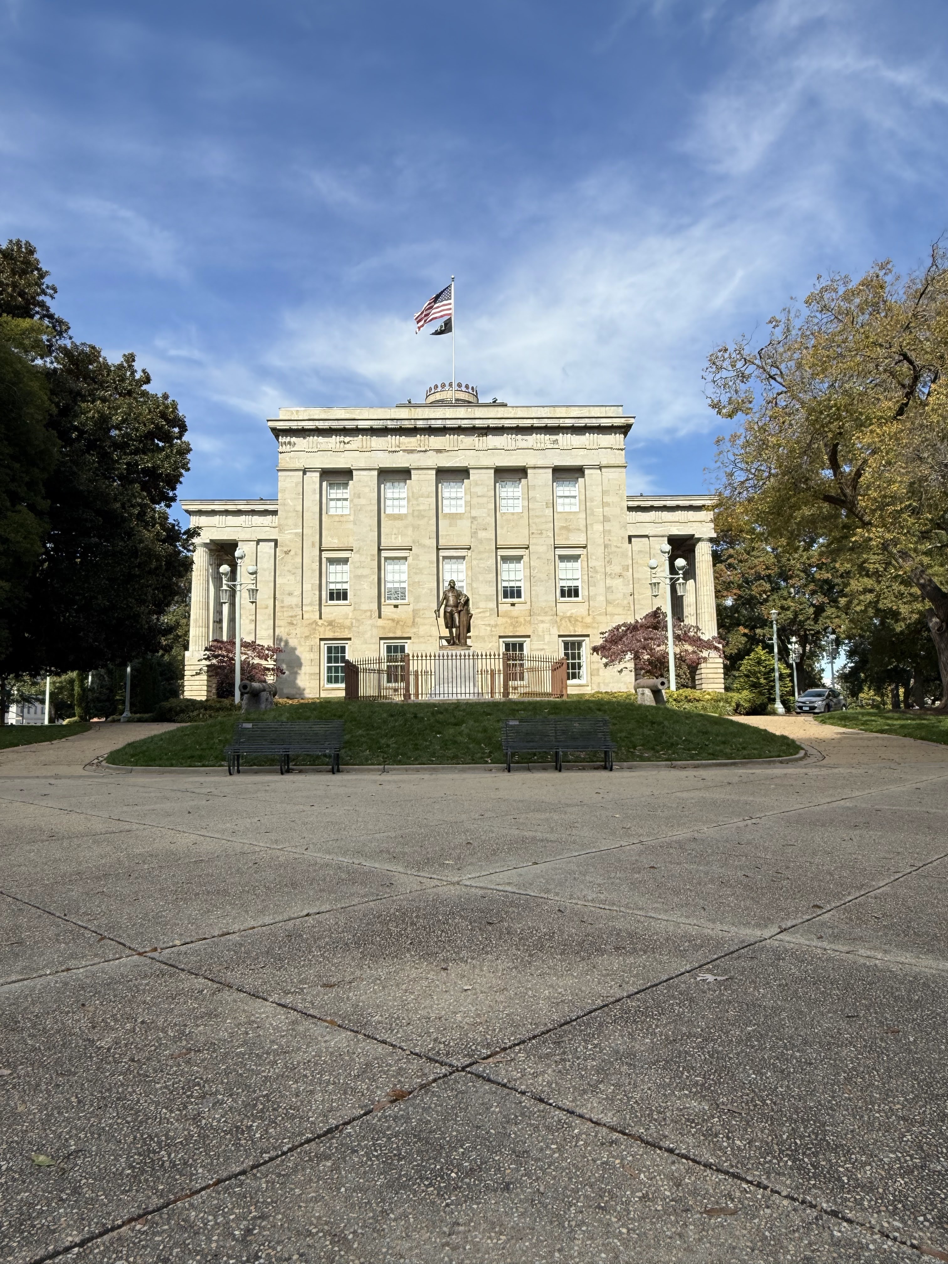 The North Carolina State Capitol rising above autumn trees and a bright blue sky in downtown Raleigh.